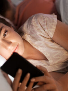 Woman laying in bed looking on her phone.