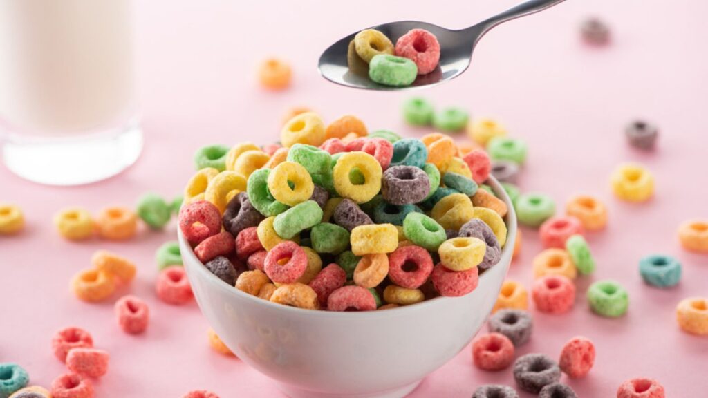 A bowl of colorful breakfast Cereal with a spoon and a glass of milk