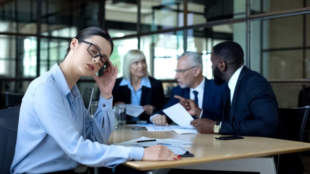 A depressed employee who is being ignored during a meeting happening in a meeting room