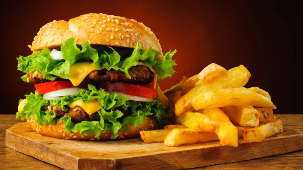 A hamburger and Fries at a Wooden Plate at a Table and Plain Background