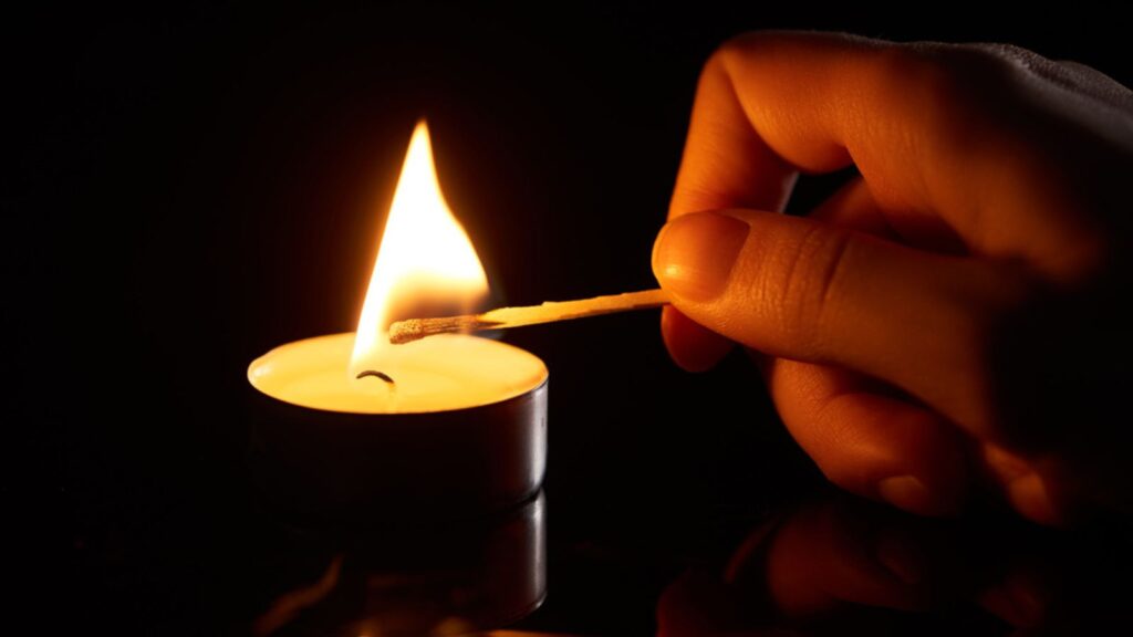 A hand of woman Holding a Burning match stick and Lightning up the candle, Dark Background