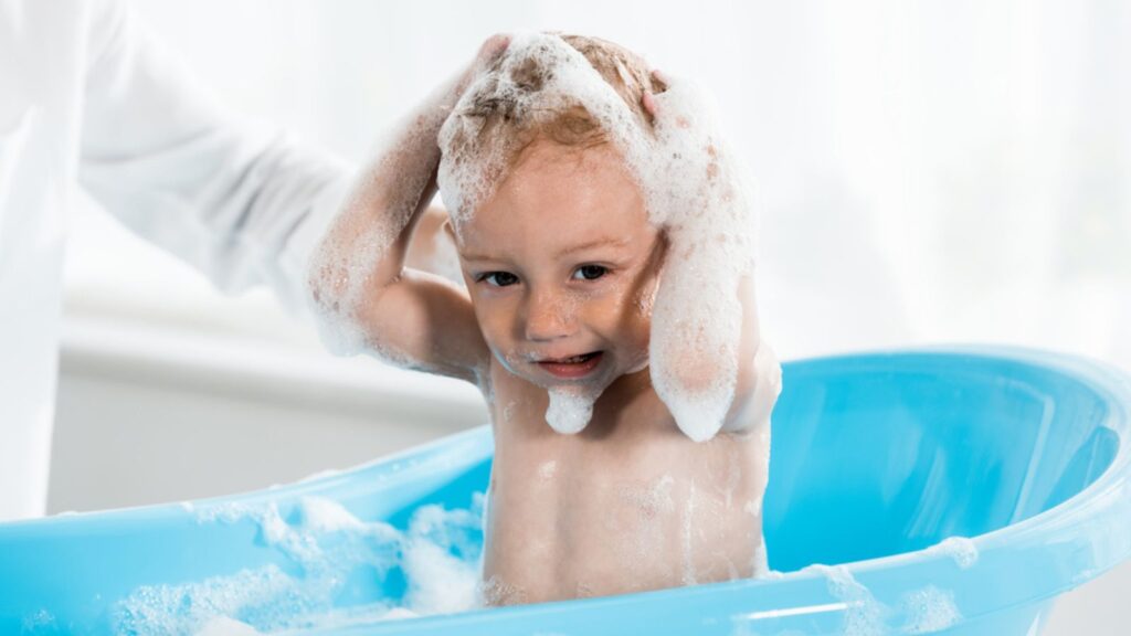 A mother applying shampoo to the head of his baby, baby sitting in the bath Tub
