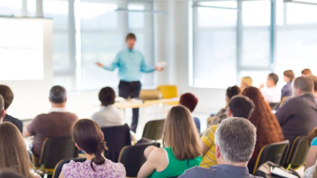A speaker speaking at a workshop, People sitting and Listening to him