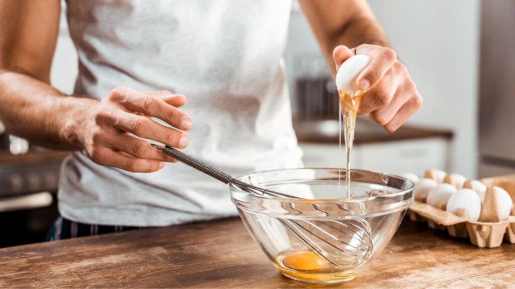 Close-up partial view of young man preparing egg omelet for breakfast