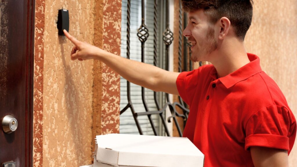 Delivery boy with cardboard pizza box near house of customer