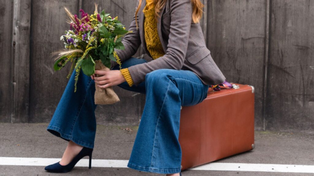 Girl sitting on vintage suitcase, Wearing bell shaped Bottoms and with a Bouquet of Flowers and a Wearing beautiful Shoes