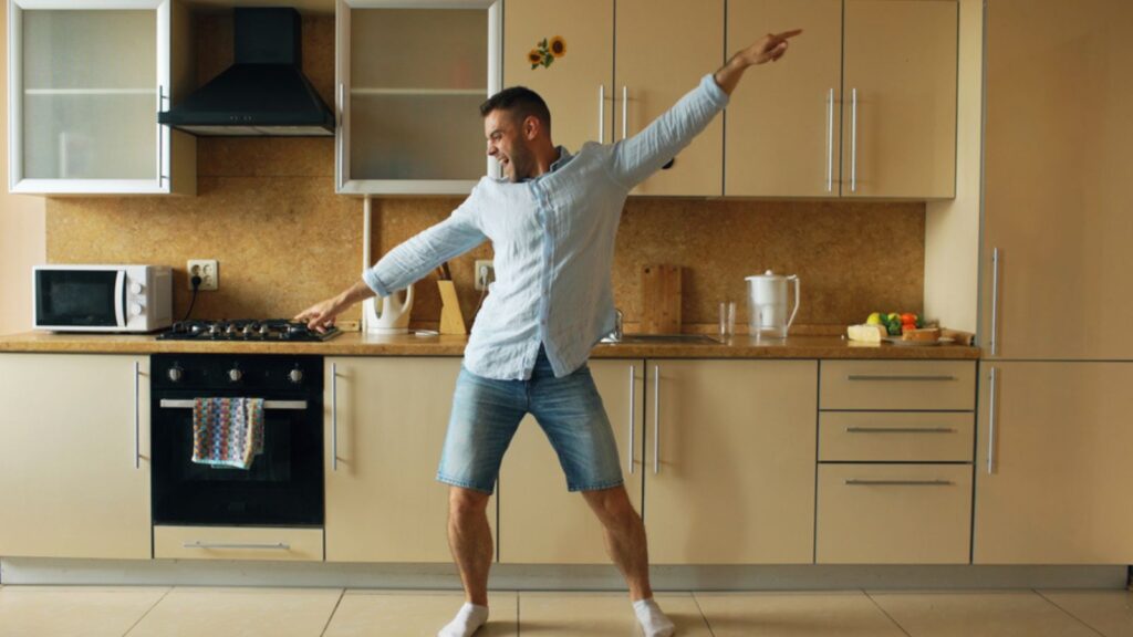 Handsome young funny man dancing alone in kitchen at home in the morning