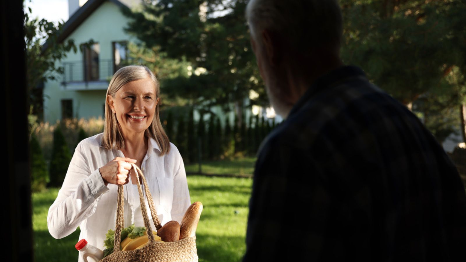 Helping neighbours. Senior woman with bag of products visiting man