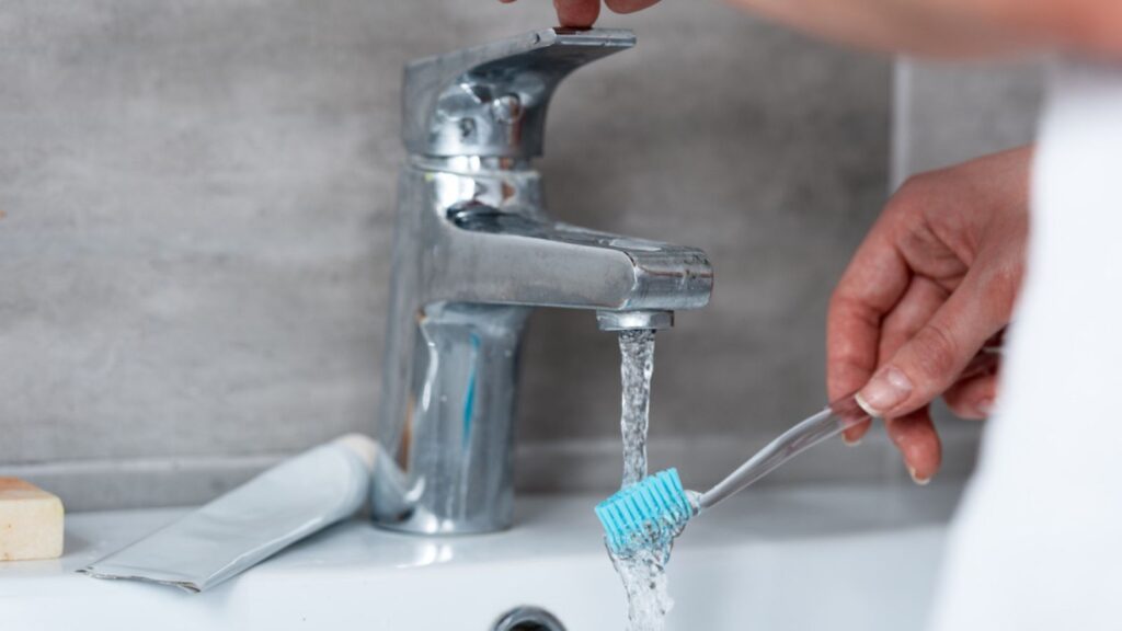 Partial view of woman wetting toothbrush in sink