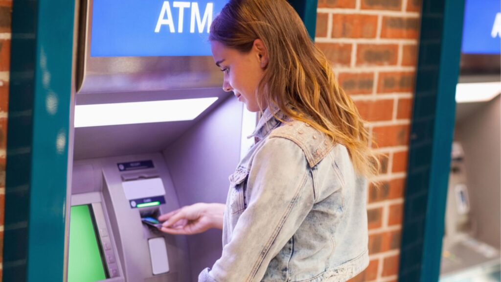 Pretty brunette student withdrawing cash with ATM Card