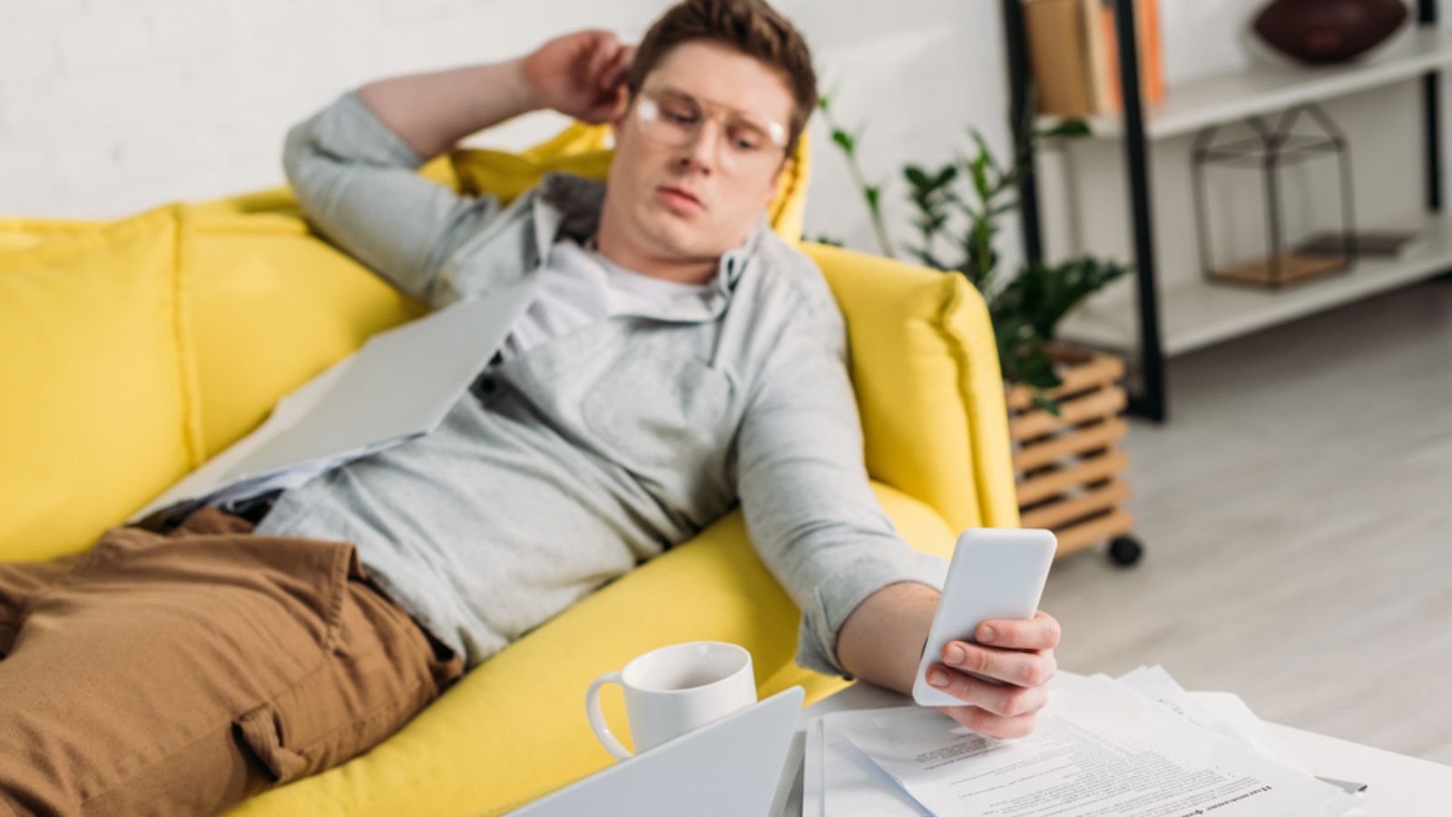 Selective focus of laptop with man using smartphone and lying on sofa