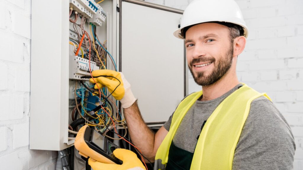 Smiling handsome electrician checking electrical box with multimeter