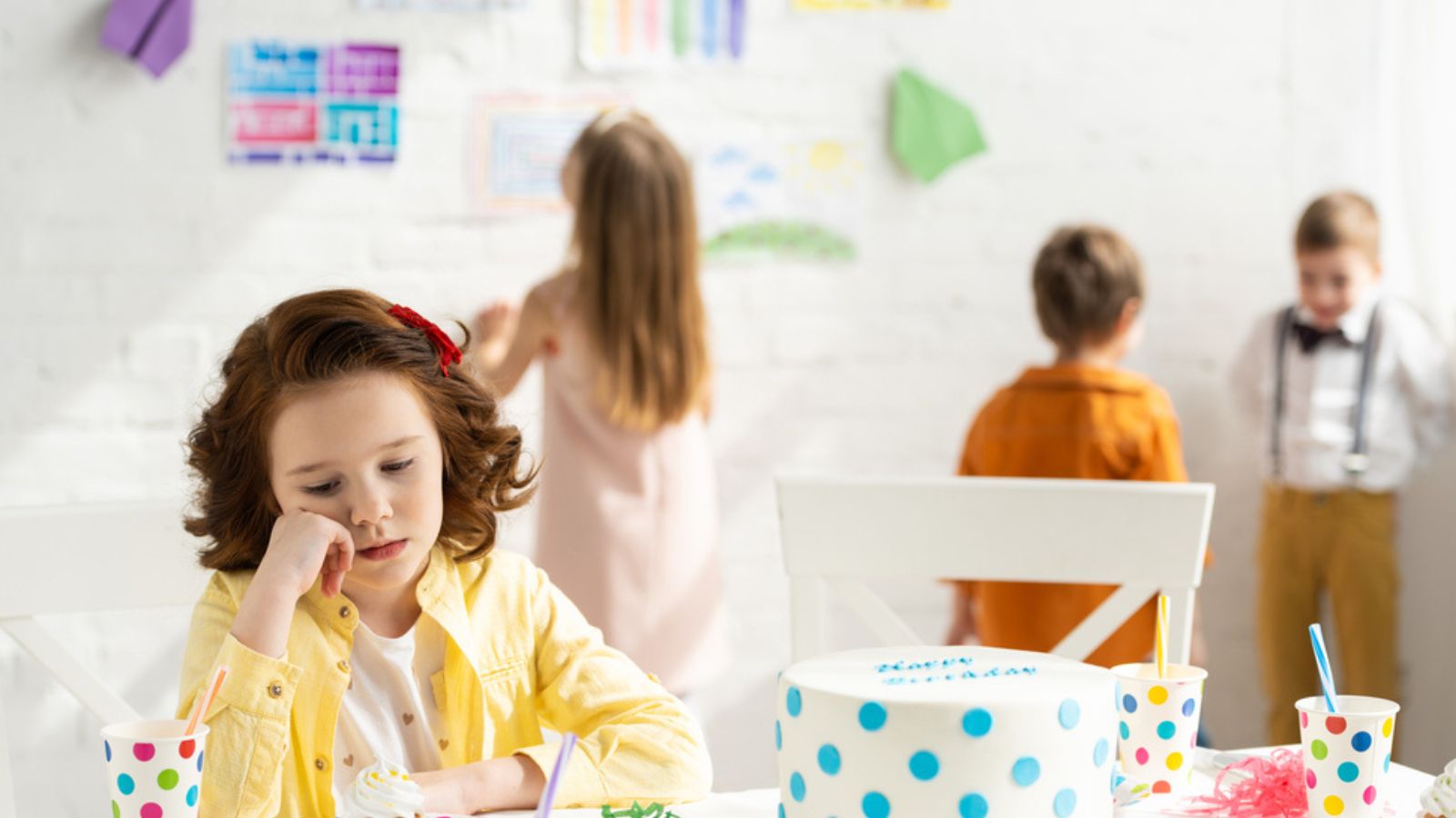 sad kid sitting at table with cake during birthday party