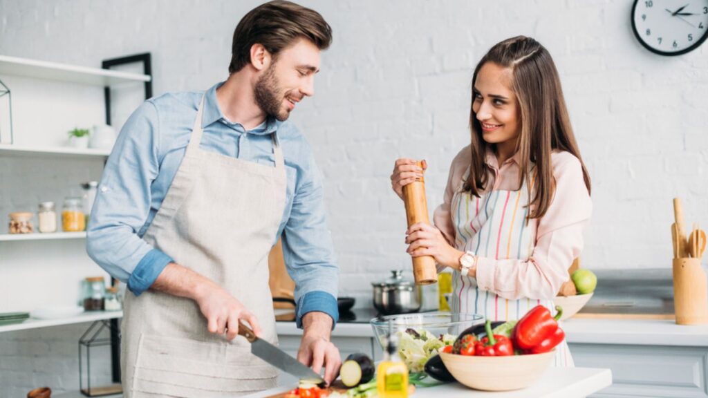 Boyfriend cutting vegetables and girlfriend adding spices to salad in kitchen
