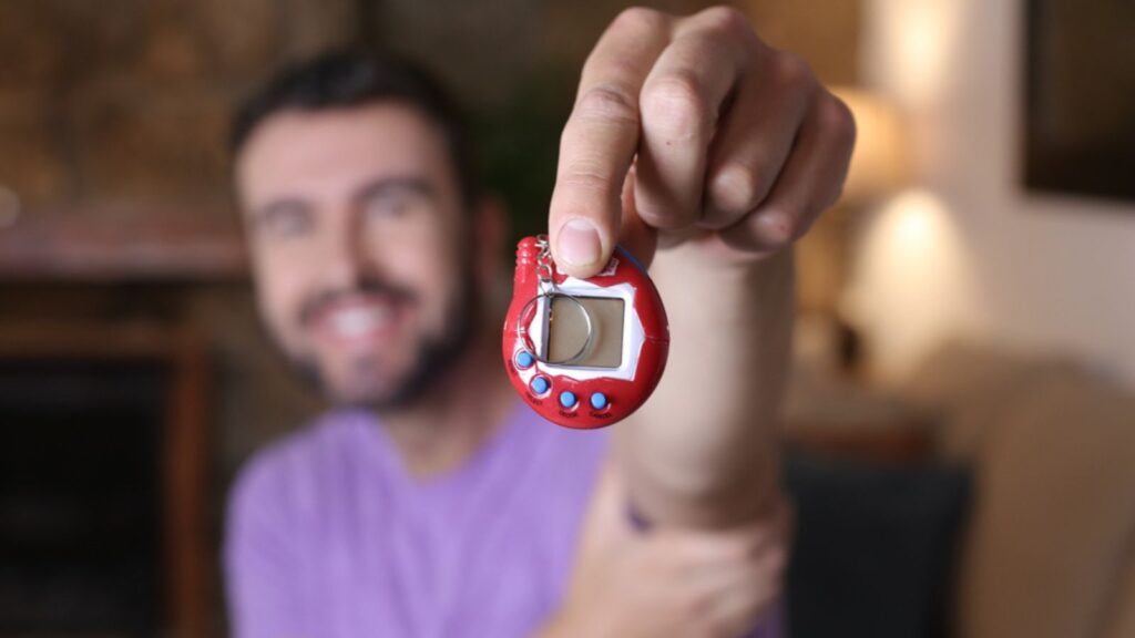 Close-up portrait of handsome young man holding Tamagotchi toy at home