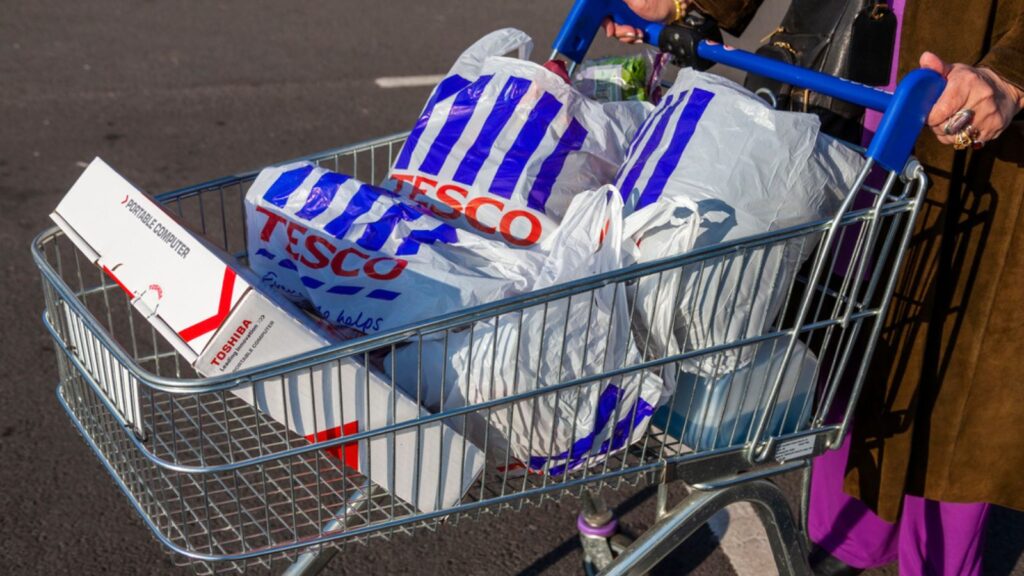 Customer shopper pushing a shopping trolley cart full of plastic carrier bags at its Tesco Extra supermarket retail business store in Brent Park Wembley stock photo