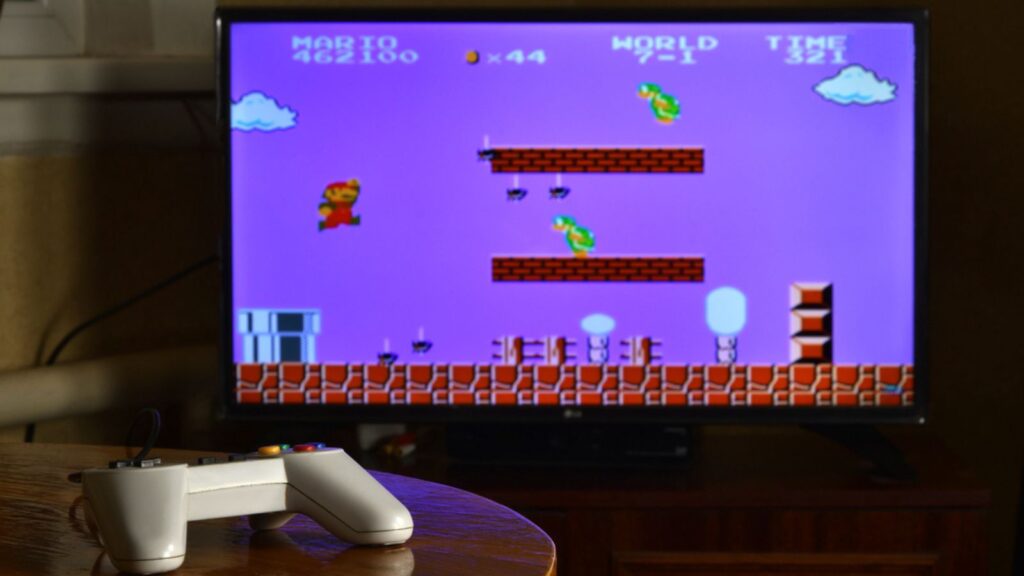 Dendy video game controller on table with Super Mario Bros game on big display
