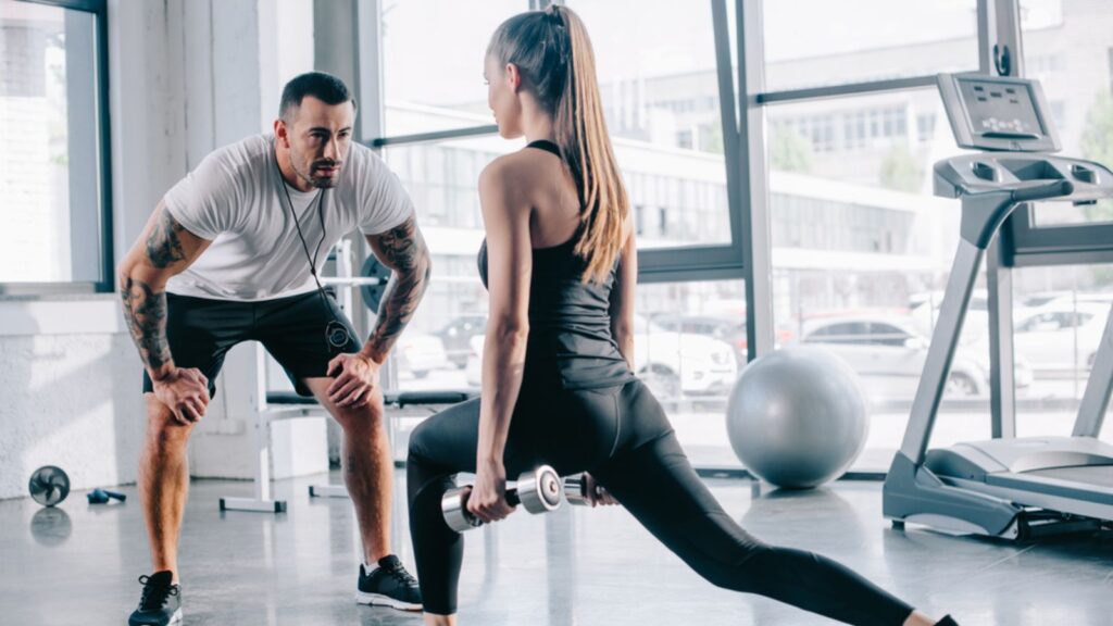 Male personal trainer looking at sportswoman doing sit ups with dumbbells'