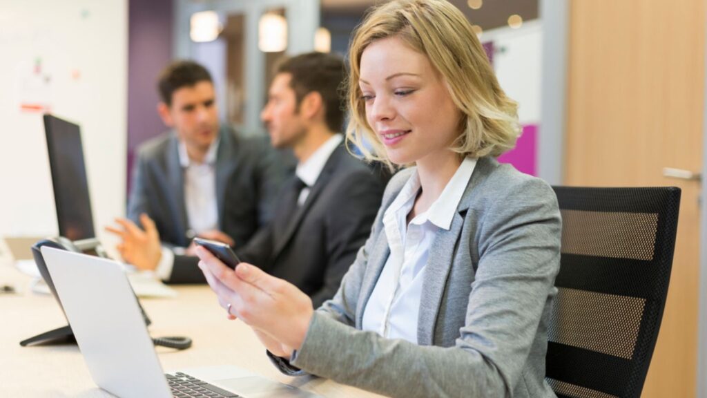 woman in her office on her phone social media distracted men talking in the background