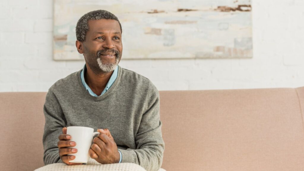 happy fulfilled man with a cup of coffee in his living room