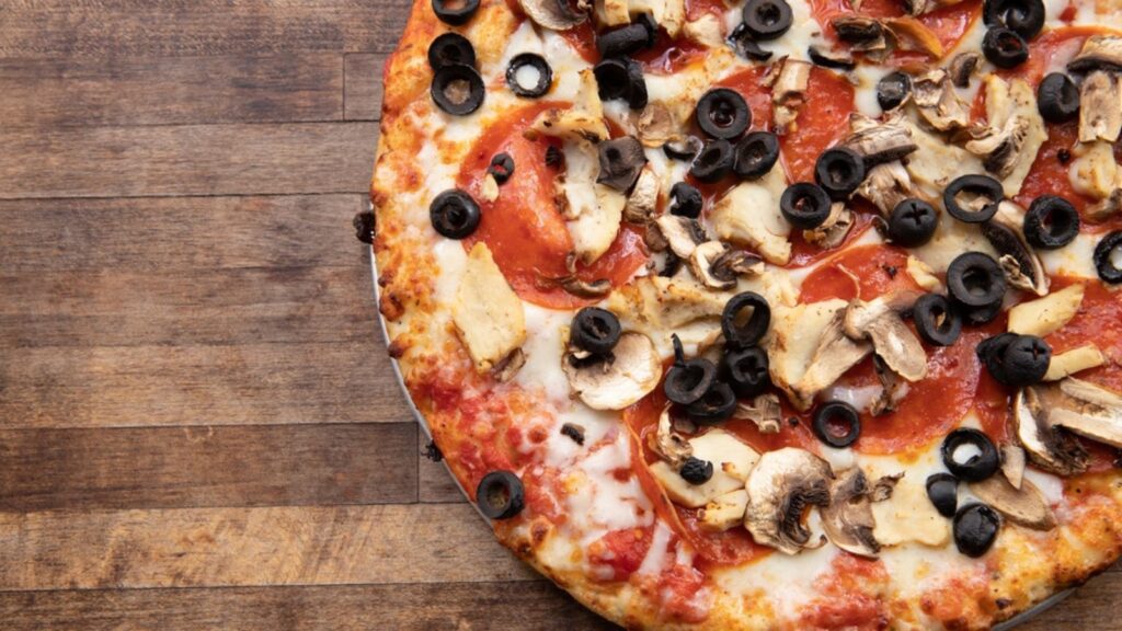 A fresh Homemade Pizza baked pepperoni, olive, mushroom and cheese pizza sits atop a decorative wooden cutting board with negative space.