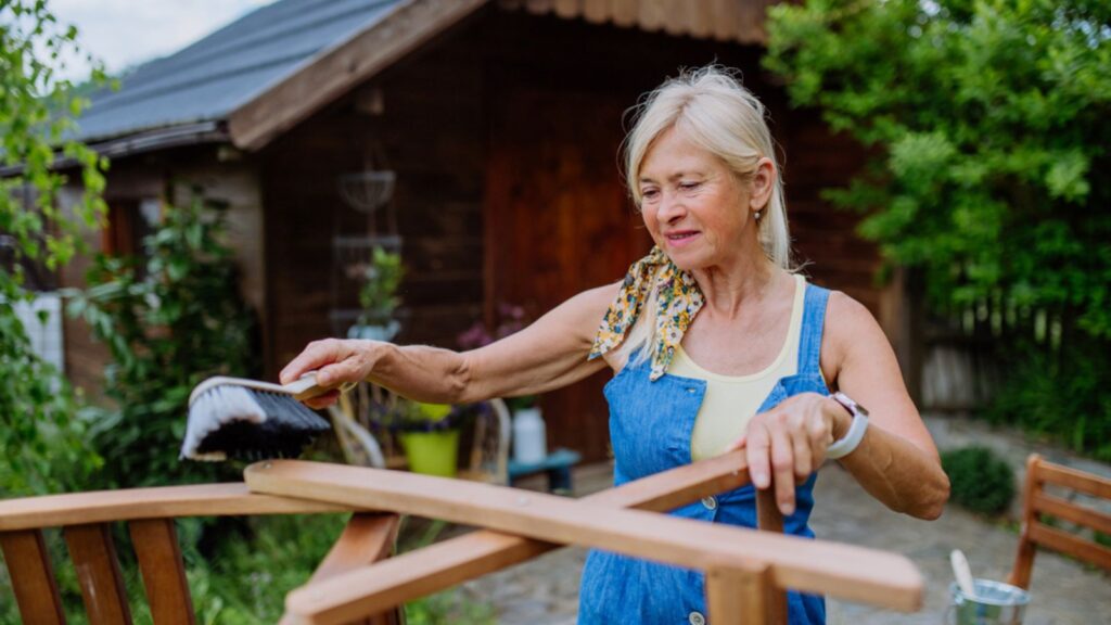_ A senior woman cleaning garden furniture and getting the garden ready