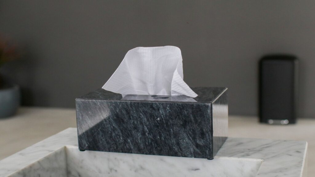 Black marble tissue box with white paper tissues. Loft style bathroom interior with modern sink.
