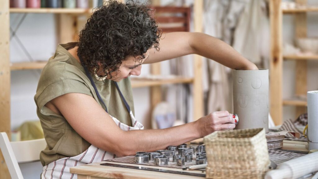 Female potter decorating a handmade ceramic vase in a pottery workshop. Hobby and craft concept.