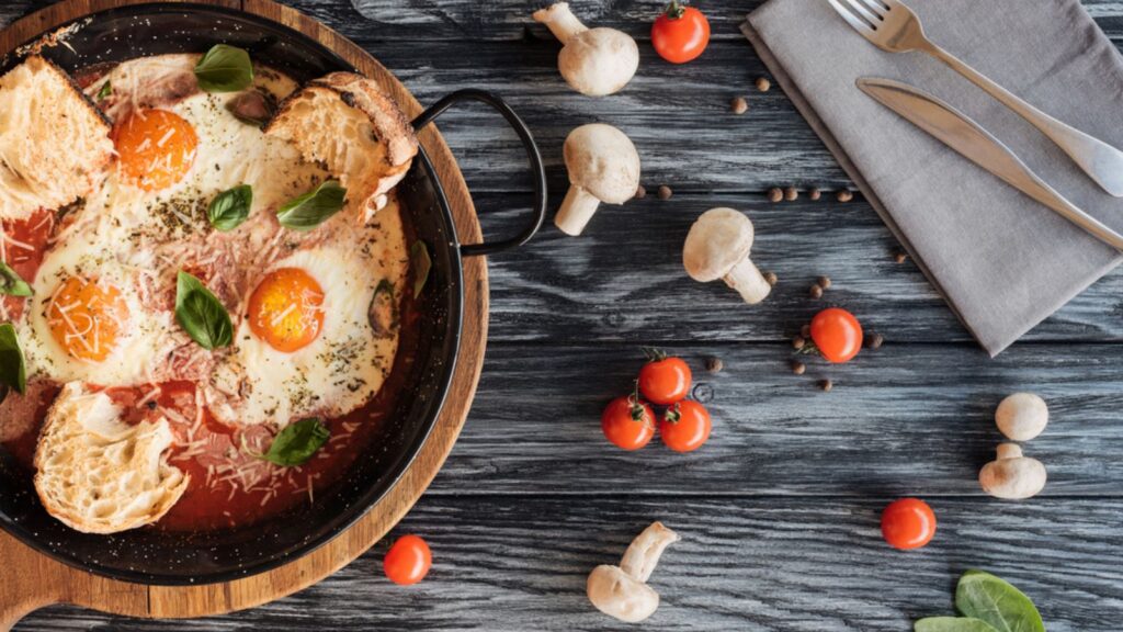 Gourmet roasted eggs with cheese, fresh vegetables and fork with knife on wooden table