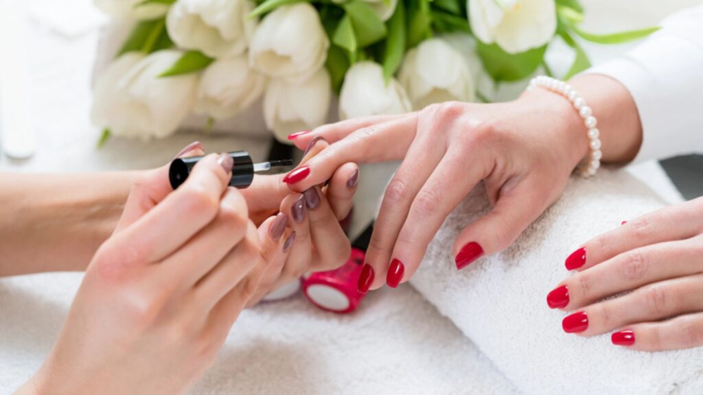 Hands of a skilled manicurist applying red nail polish on the nails