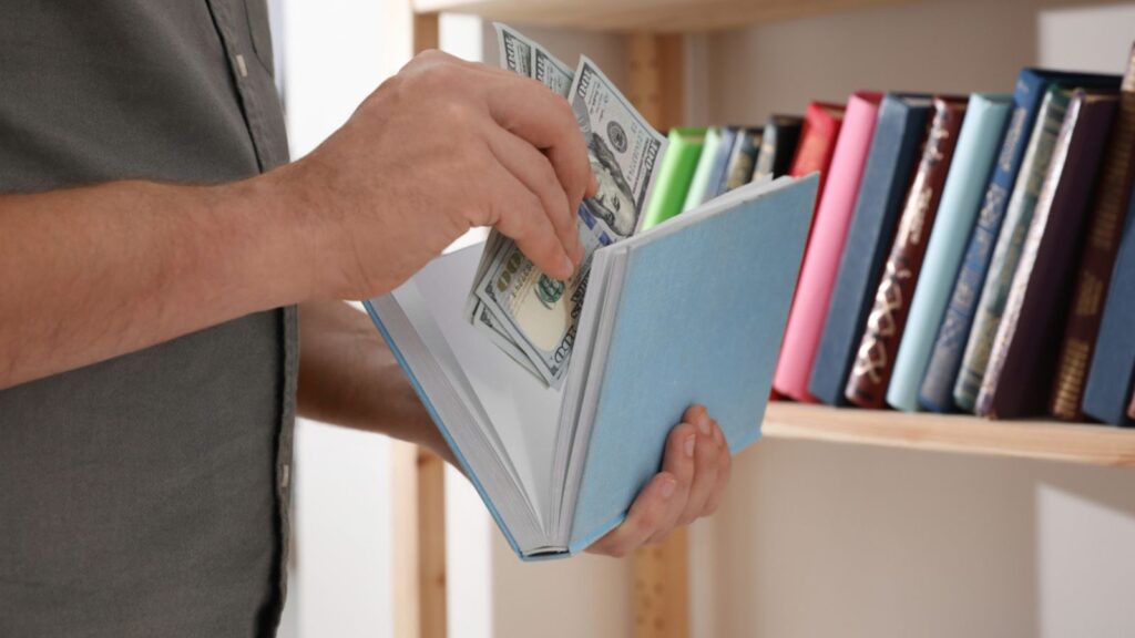 Man hiding money in book indoors, closeup.
