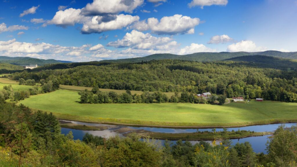 River meanders through the pastures lush green country side in the summer time of the state Vermont
