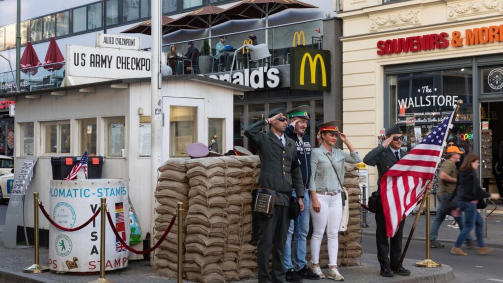 Tourists taking souvenir photo with men in former American military uniforms during the Cold War at the Checkpoint Charlie in Berlin, Germany.