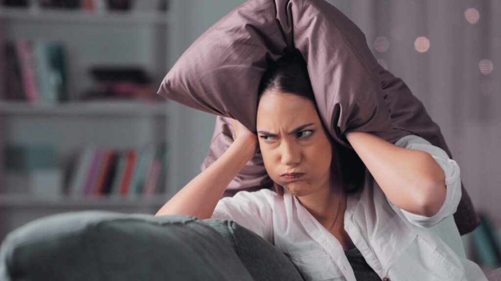 frustrated annoyed woman holding a pillow over her ears