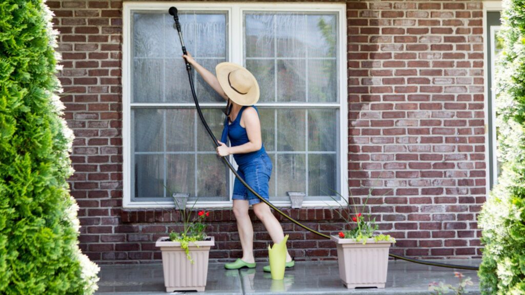 woman in her garden yard cleaning her windows brick house
