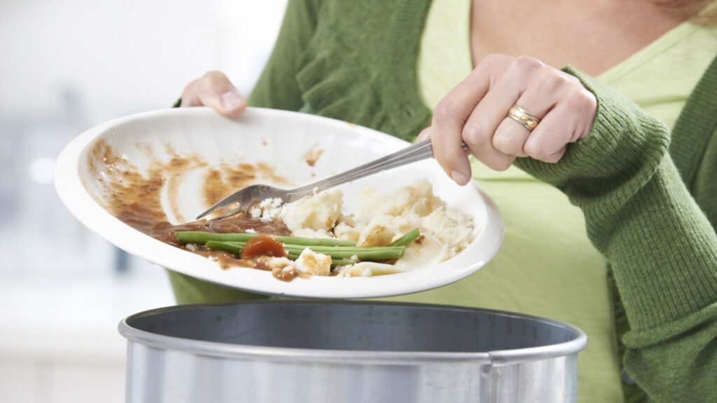 Woman Scraping Food Leftovers Into Garbage Bin