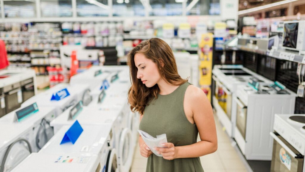 Woman buys washing machine in a store, holding manual.