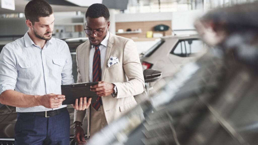 A young black businesswoman signs documents and buys a new car. The car dealer is standing next to him.