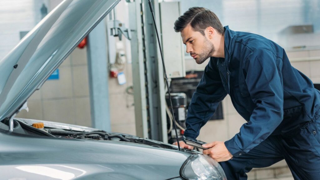 Automechanic looking under car hood repairing car