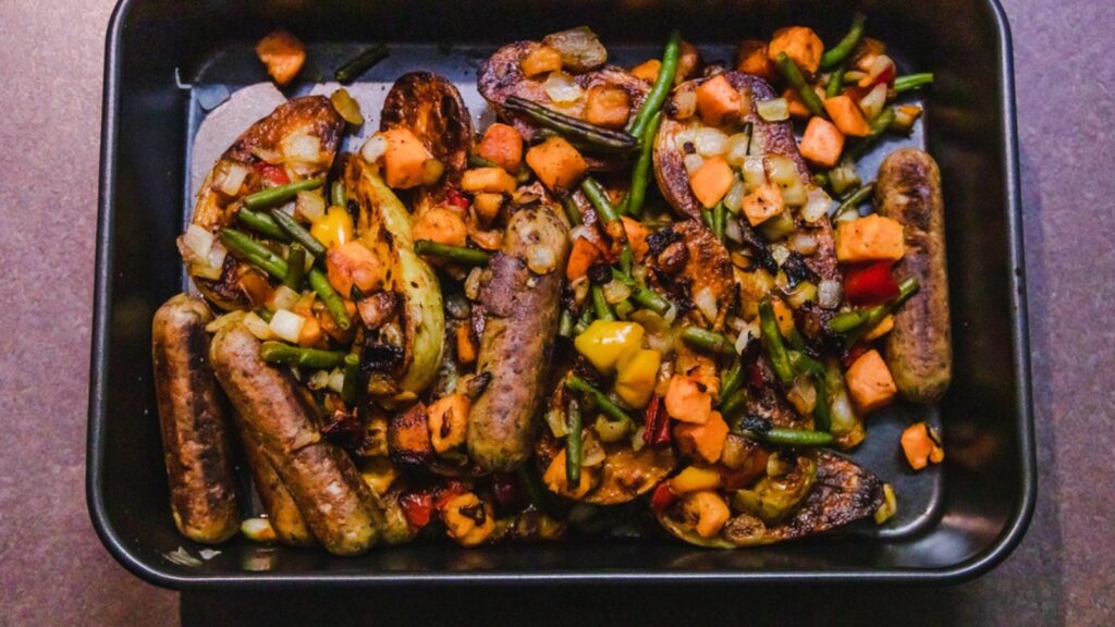Baking tray with vegan sausages potatoes and mixed roasted veggi