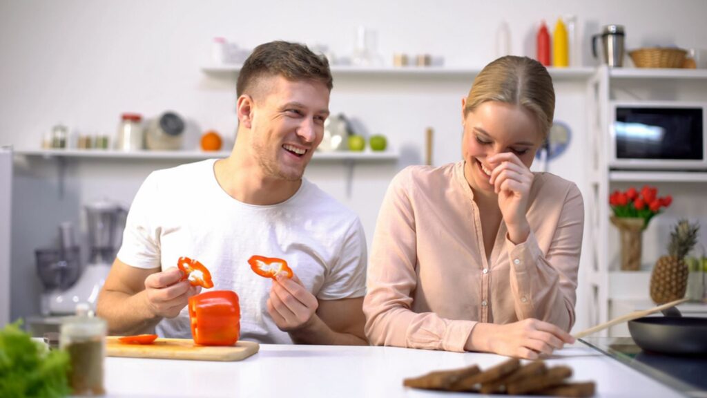 Cheerful couple fooling around at kitchen and laughing, having fun together