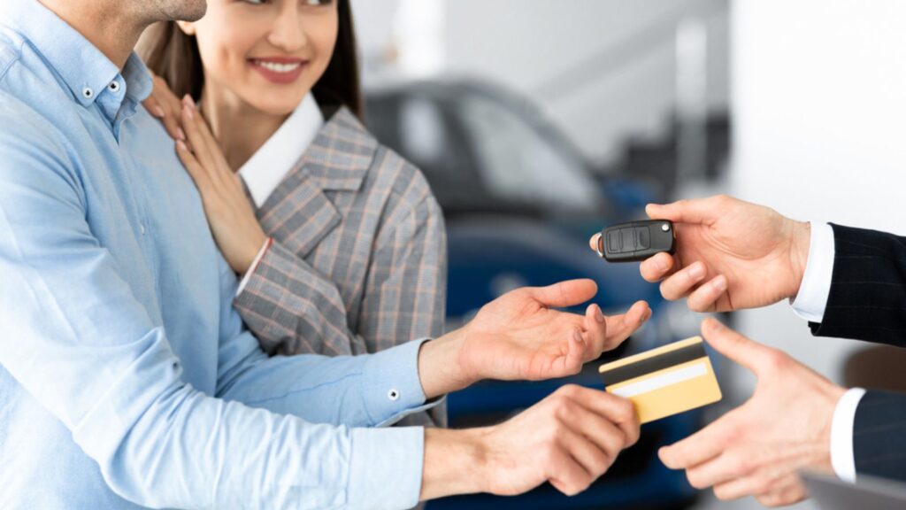 Couple Buying Car Giving Seller Credit Card In Dealership Office