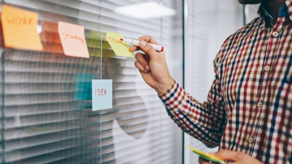 Crop anonymous man in casual outfit writing ideas with red