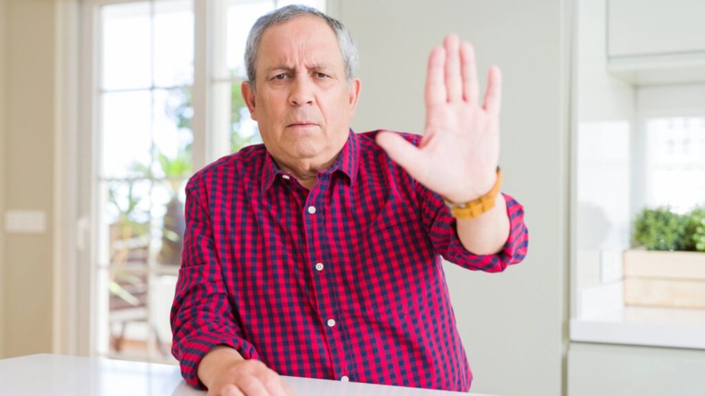 Handsome senior man at home doing stop sing with palm of the hand saying no