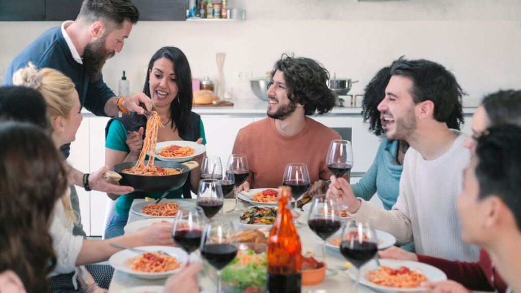 Happy group of friends eating pasta at home dinner party