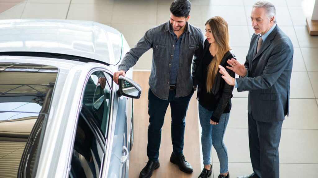 Happy young family talking to the salesman and choosing their new car in a showroom