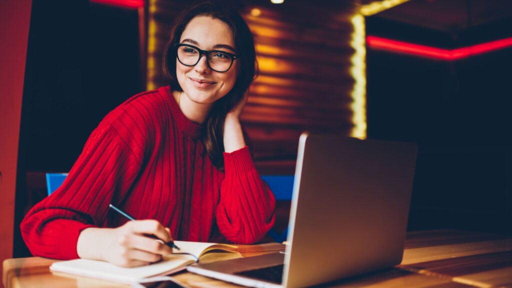 happy woman working at her computer glasses writing journal