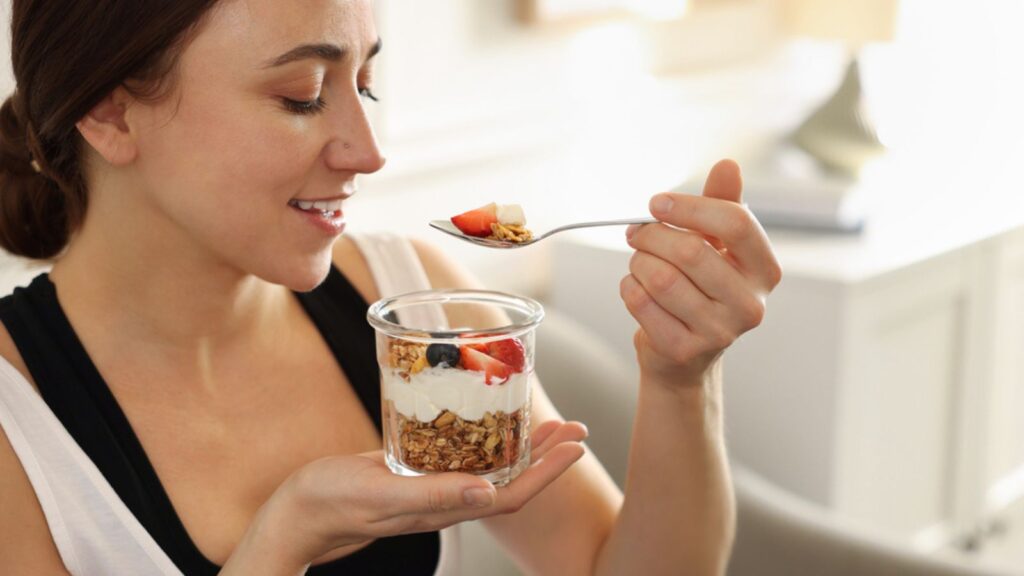 Woman eating tasty granola with fresh berries and yogurt at home
