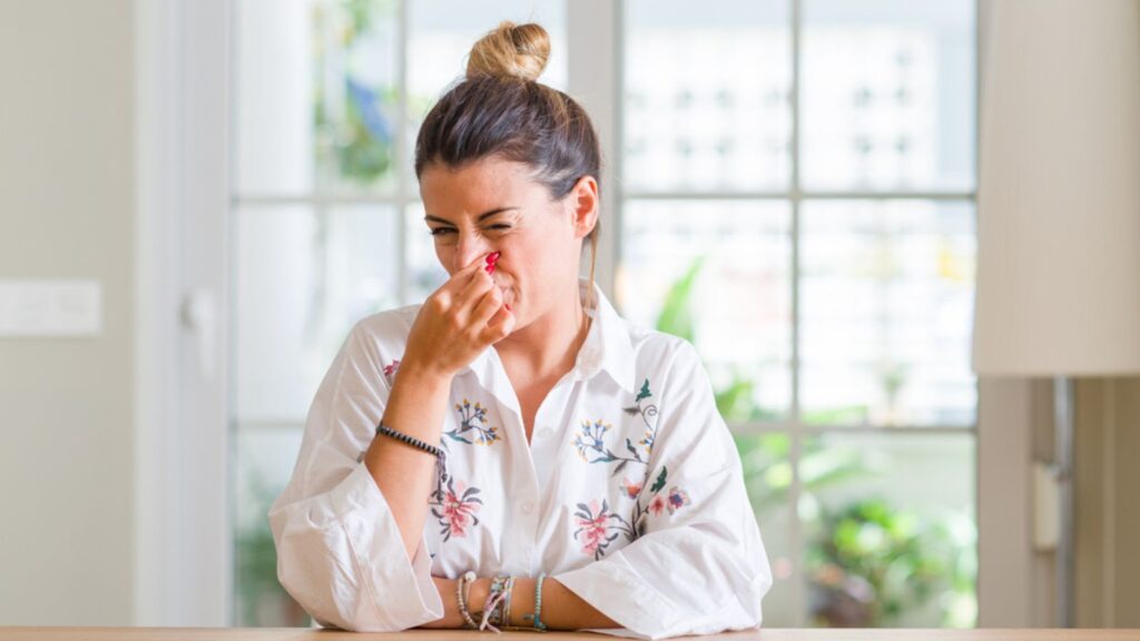 Young woman at home smelling something stinky and disgusting,