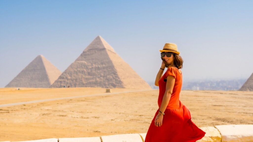 A tourist woman in a red dress at the Pyramids of Giza, the oldest Funerary monument in the world. In the city of Cairo, Egypt